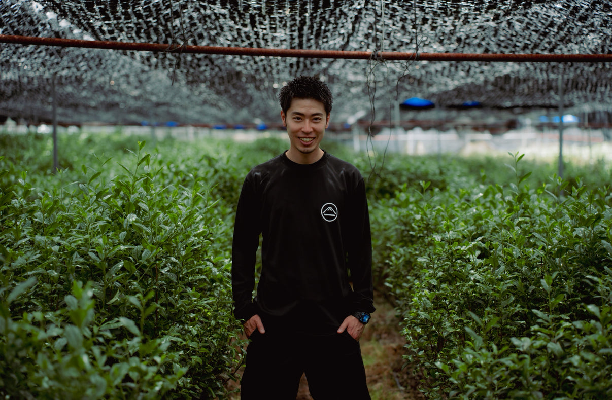 Person standing in a field with greenery and a netted structure in the background