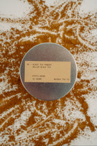 Round metal container with a label on a surface with scattered tea leaves