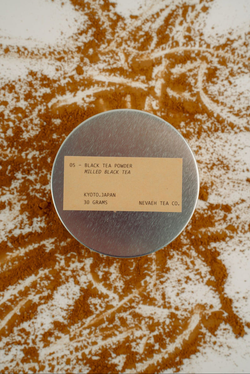Round metal container with a label on a surface with scattered tea leaves