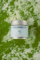 Okumidori matcha container on a green and white textured background