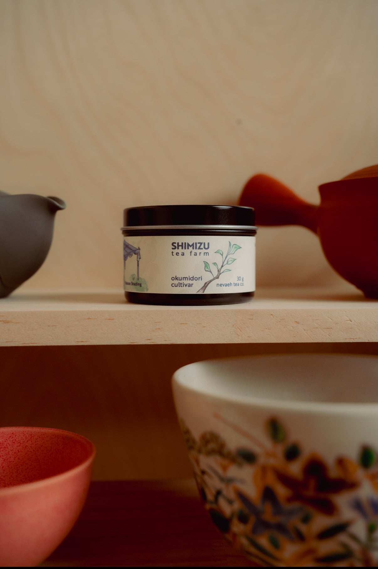Jar of Shimizu tea on a wooden shelf with tea-making utensils.