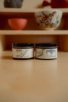 Two small containers with labels on a wooden surface with blurred background